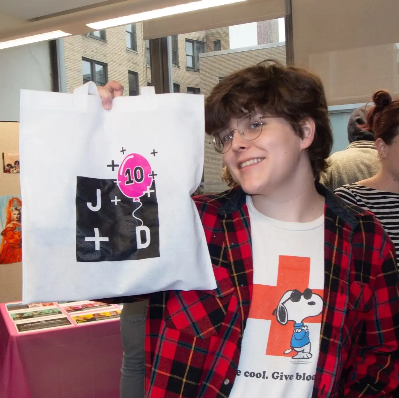 A photo of me holding up a tote bag with the Journalism + Design 10 year anniversary logo on it.